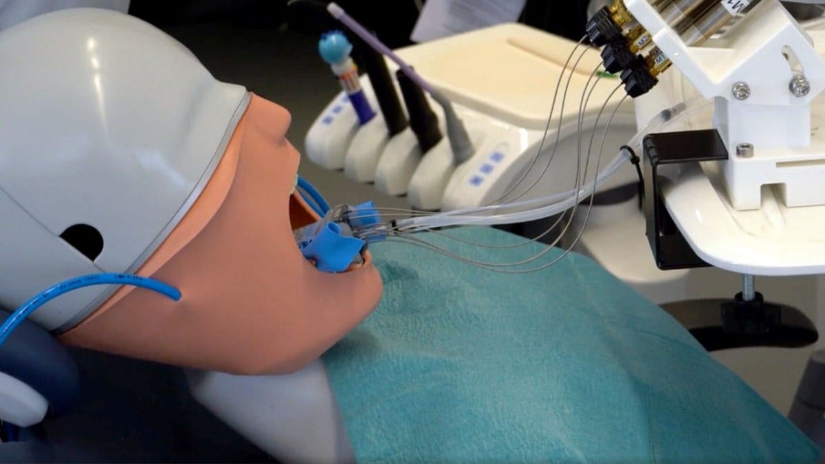 Small cylindrical dental robot prototype next to synthetic tooth model in university laboratory setting