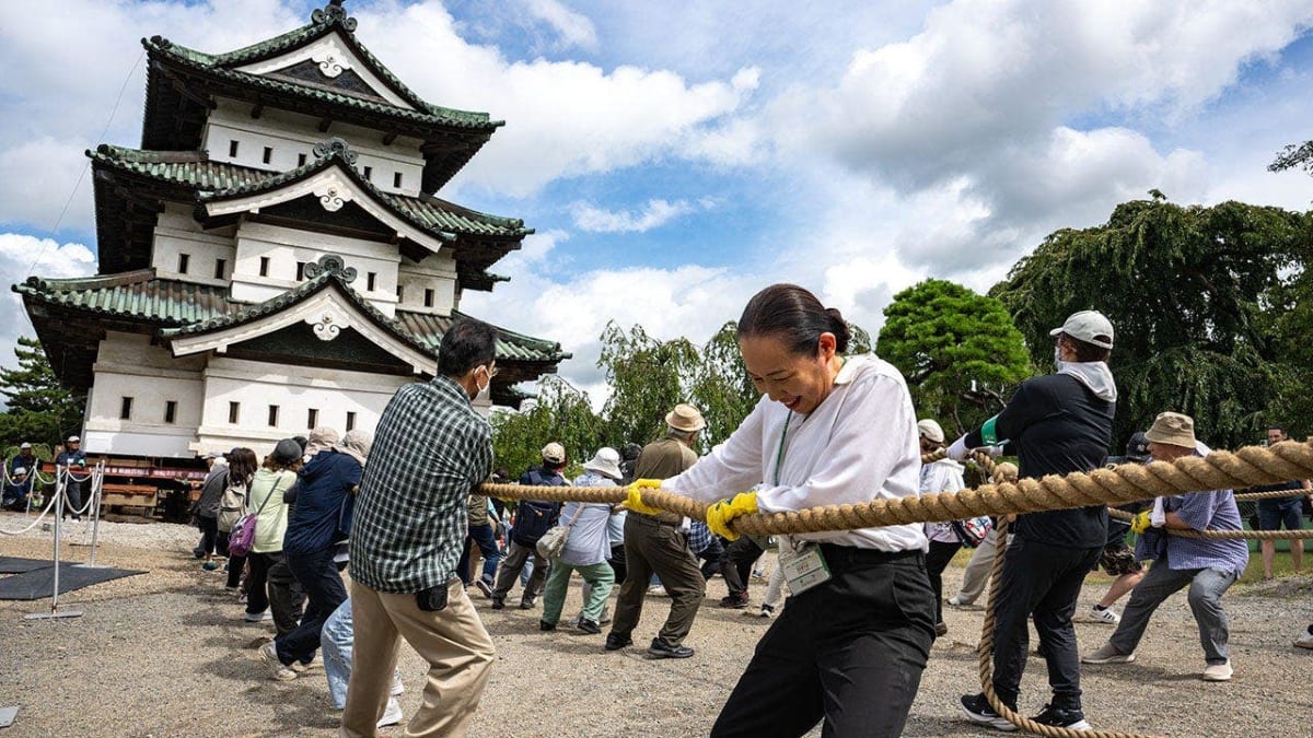 Large crowd pulling Hirosaki Castle tower with ropes across wooden rollers in Japan