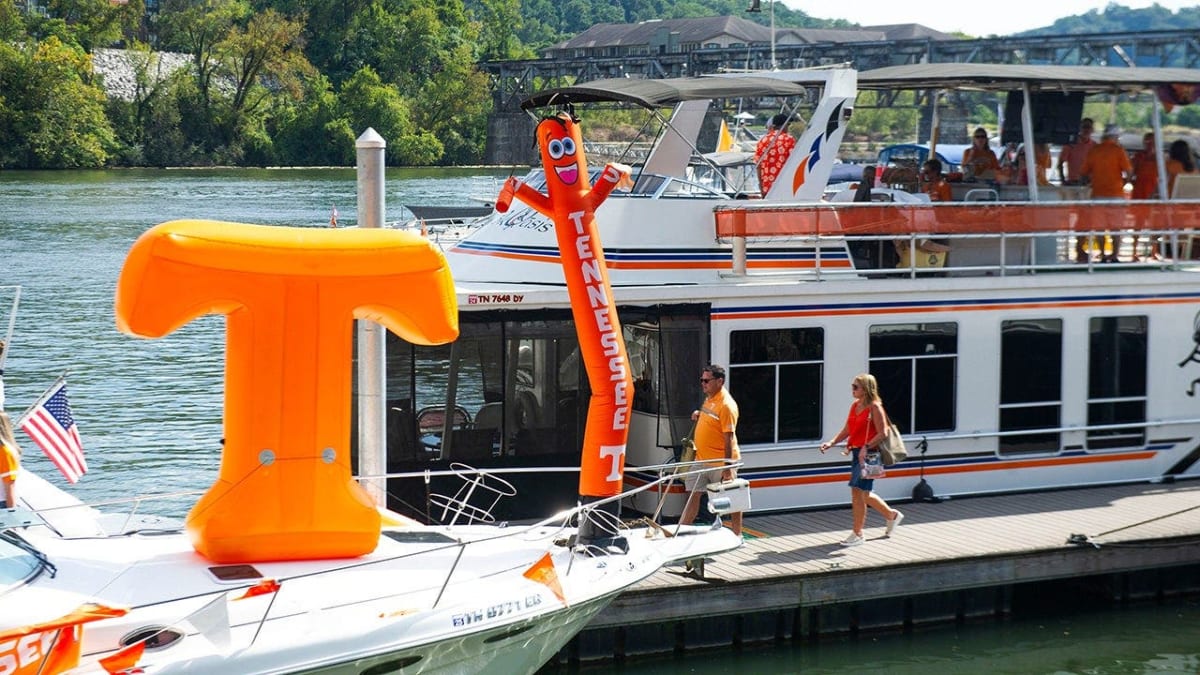 ** Boats lined up along waterfront near football stadium with fans tailgating on decks