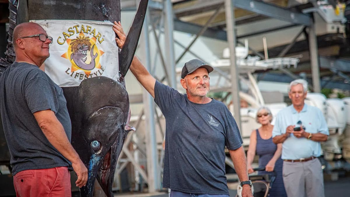Two fishermen pose beside enormous blue marlin hanging at dock in Falmouth, Massachusetts