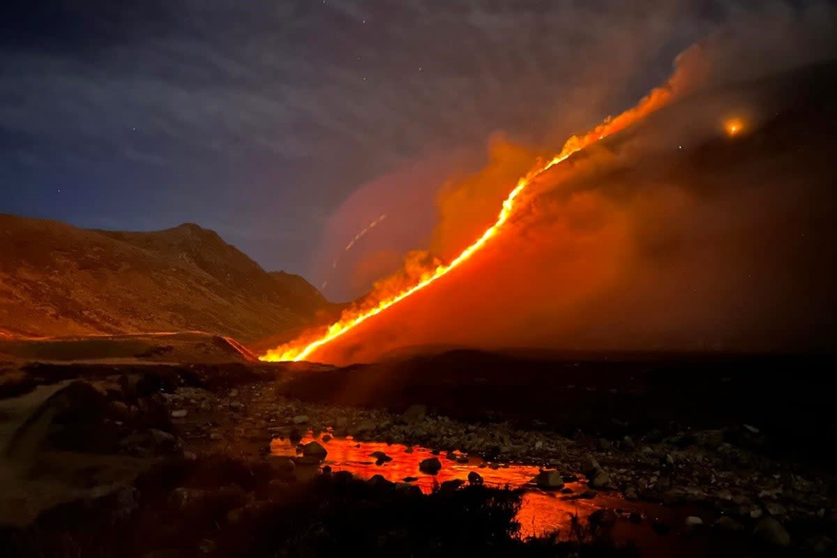 Firefighters battling wildfire across moorland with equipment and vehicles visible in landscape