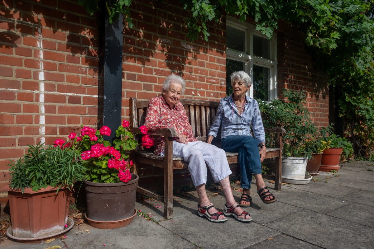 Elderly woman standing beside colorful potted plants and wooden bench on London street