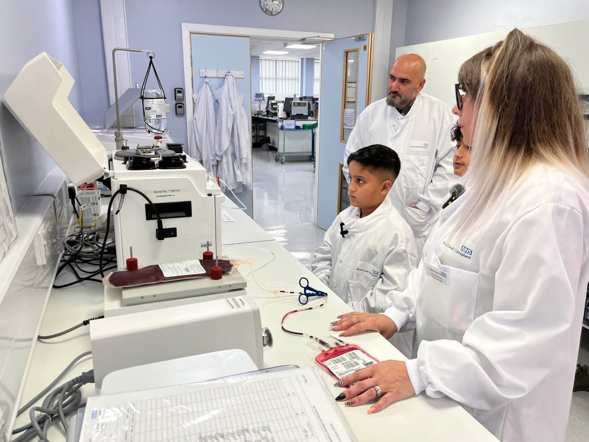 Nine-year-old Qasim Rizwan smiling in oversized lab coat at NHS blood bank facility