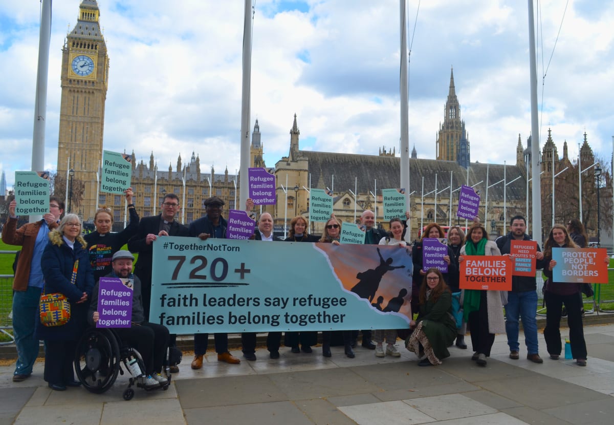Faith leaders of different religions gathering outside UK Parliament building holding signs about refugee families