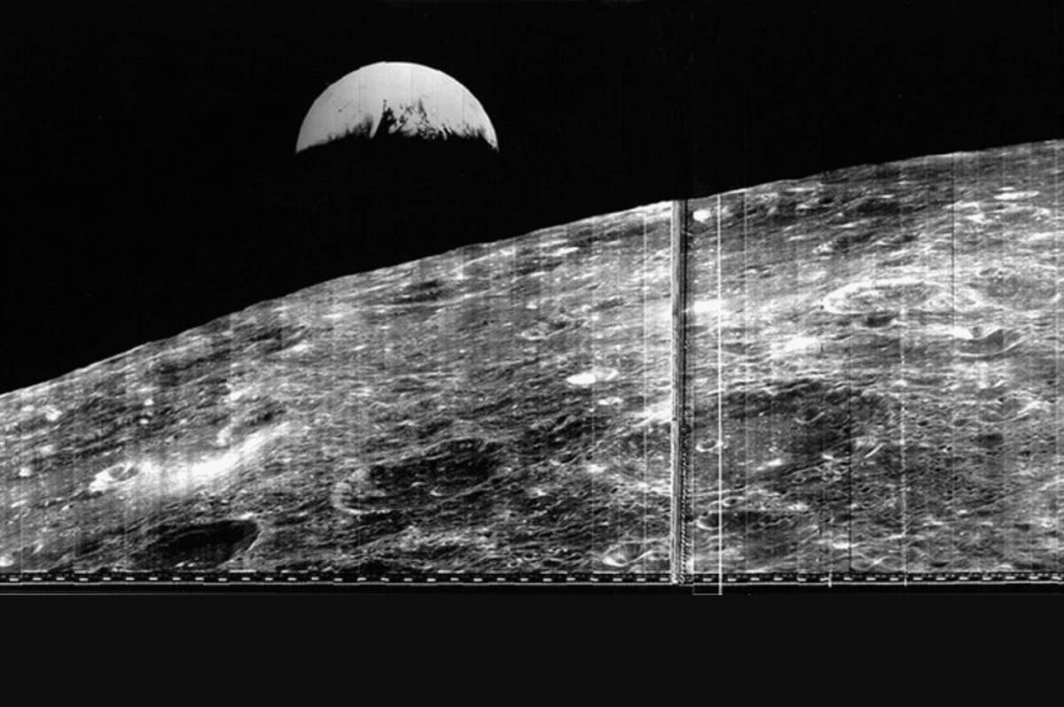 Black and white photograph showing Earth as semicircle above moon's cratered surface from space