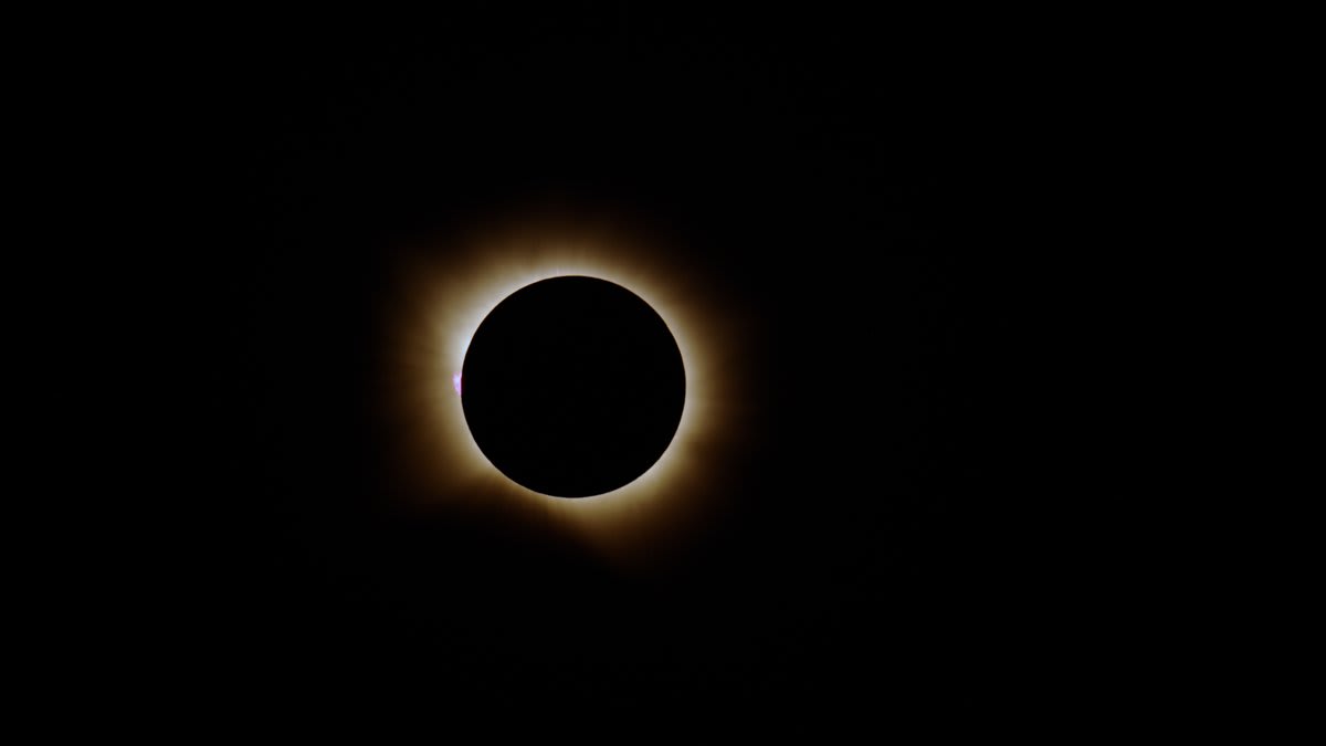 4K time-lapse showing total solar eclipse with white corona surrounding dark moon and red solar prominence