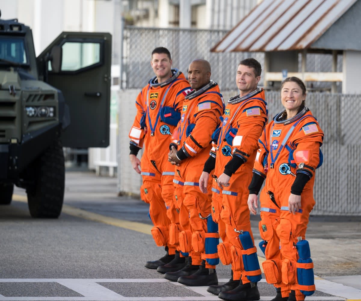 Four Artemis II astronauts in orange flight suits standing together before historic moon mission