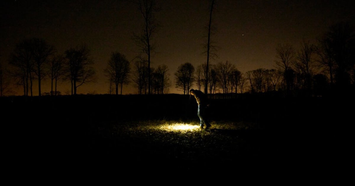 Man examining small black meteorite fragment on ground in Ohio field