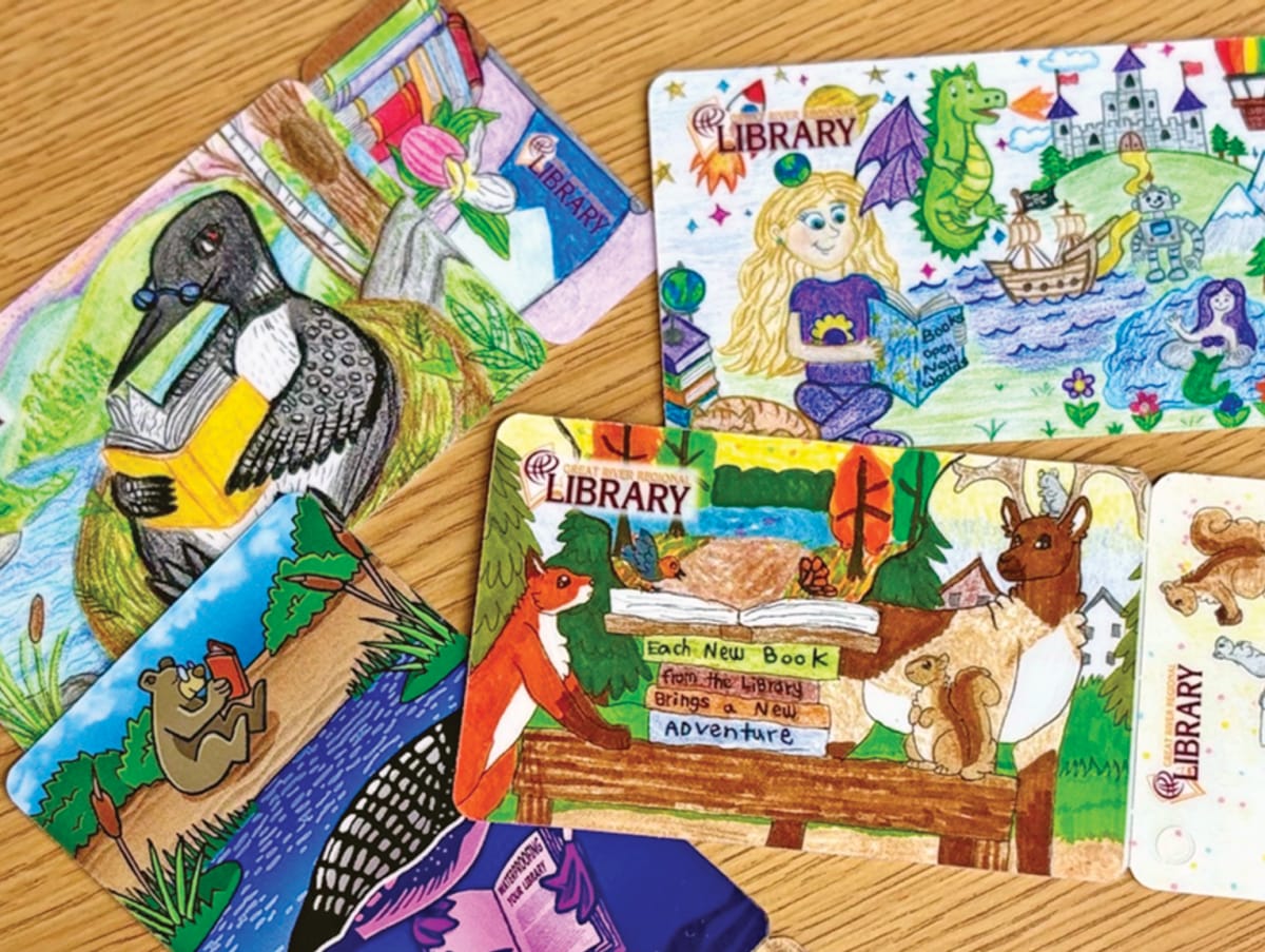 Children's hands holding colorful new library cards featuring winning artwork designs from regional contest