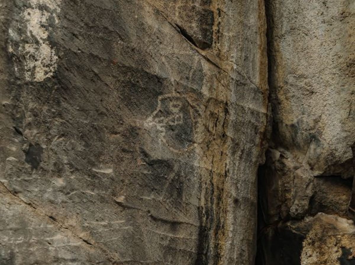 Ancient red rock painting showing prehistoric figure holding snake or lightning bolt on cliff face