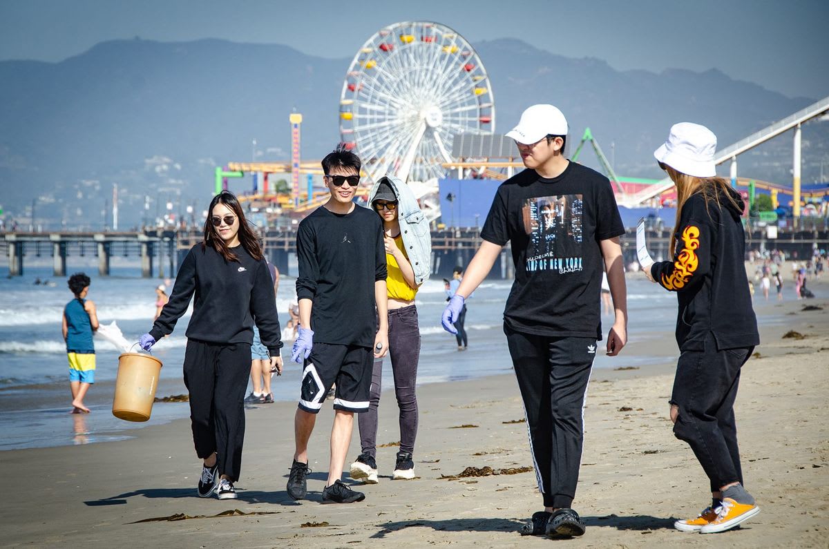 Volunteers cleaning sandy beach with ocean waves in background at historic Santa Monica location