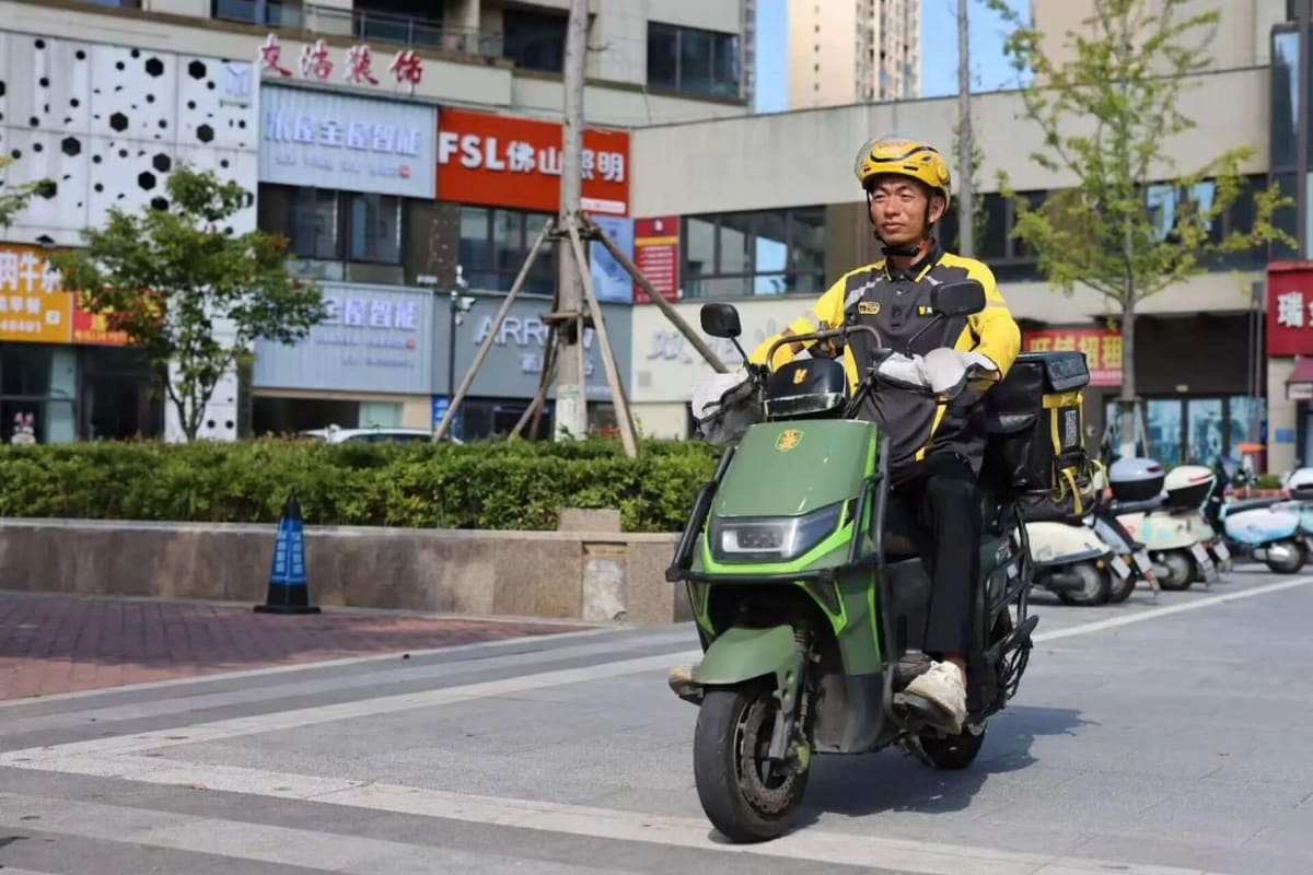 Food delivery rider on electric scooter checking smartphone while wearing helmet and uniform