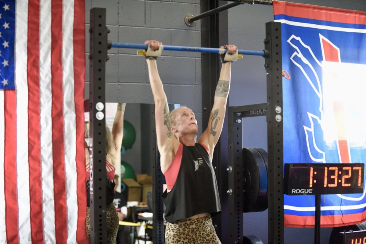 Woman in athletic wear performing pull-up on bar with supporters watching nearby