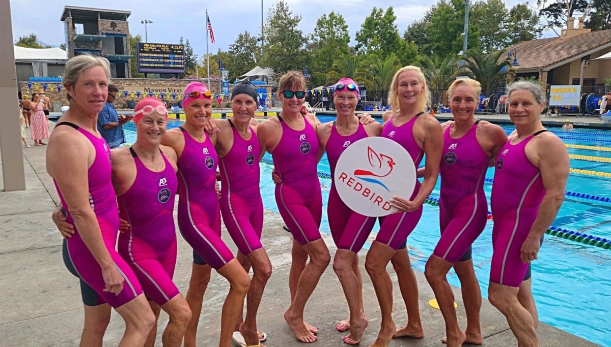 Team Redbird women swimmers celebrating together poolside after breaking multiple world records