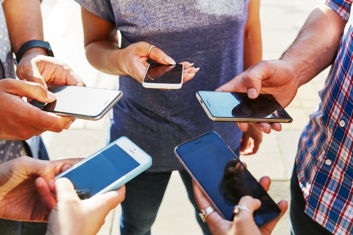 Group of diverse friends laughing together at outdoor cafe table using smartphones