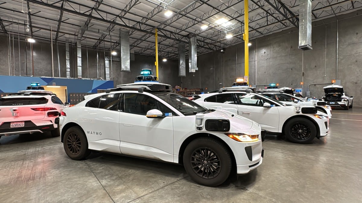 White Waymo self-driving electric vehicle on city street with charging infrastructure visible