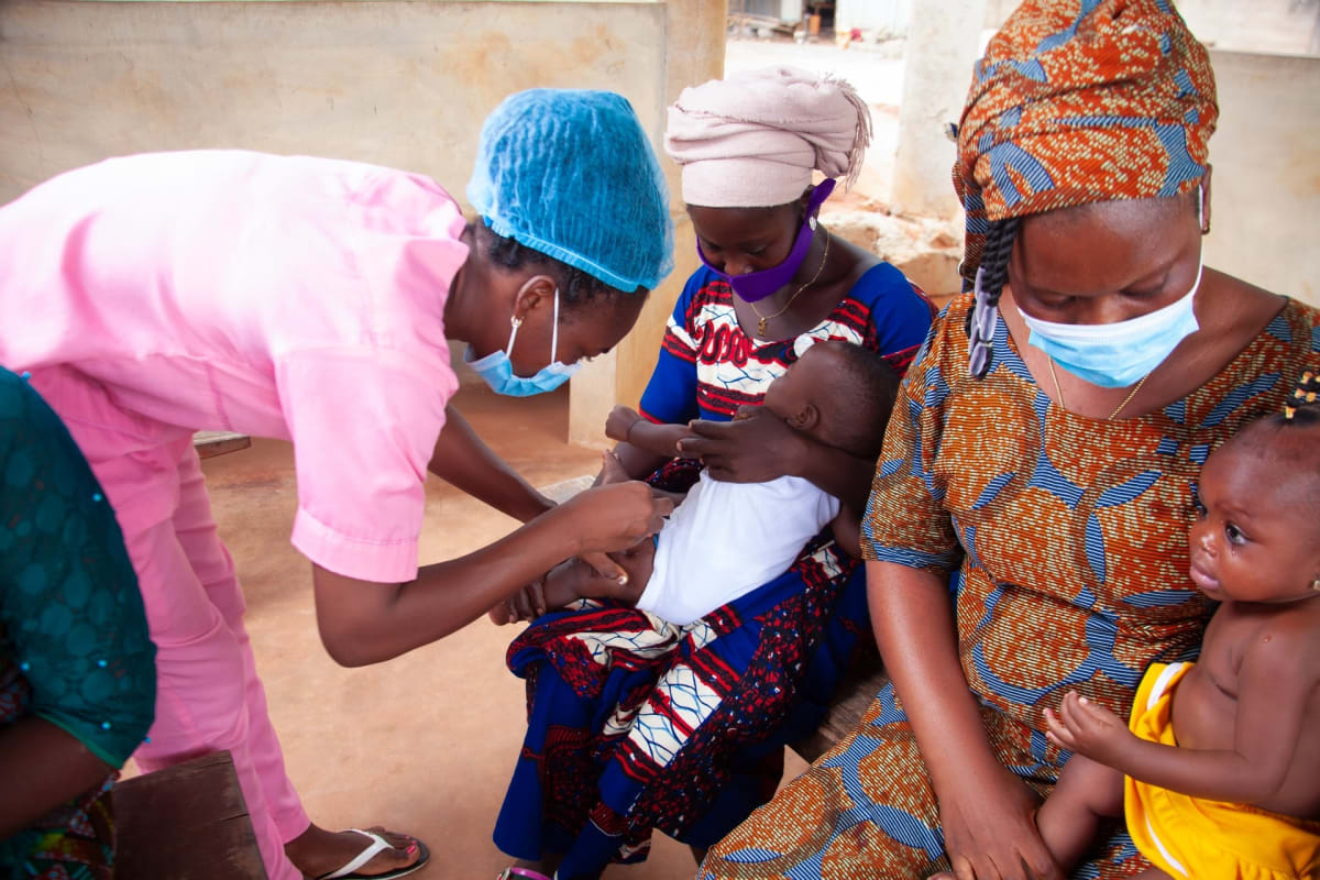 ** Healthcare workers assisting patient in Nigerian hospital with digital fundraising platform displayed on screen