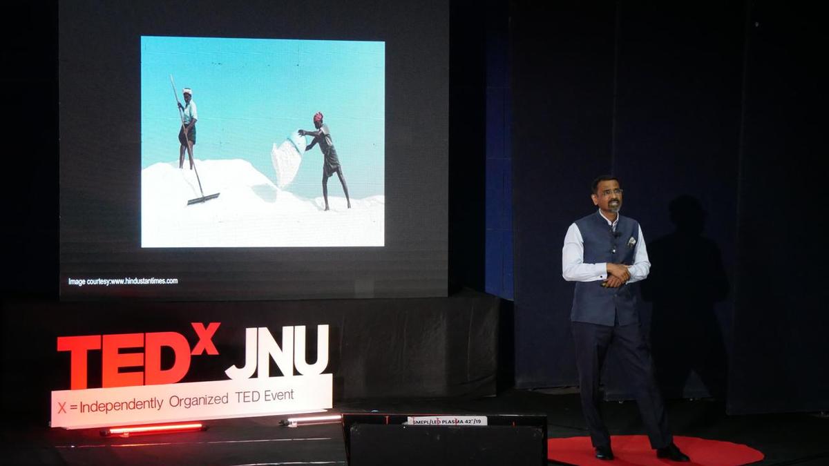 Speaker K. M. Pathi presenting at TEDx talk in Jaipur auditorium with red circular logo backdrop