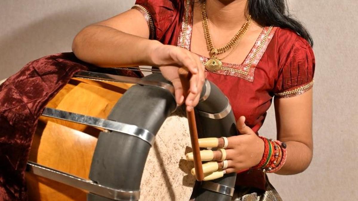 Young woman in traditional attire plays large thavil drum balanced on her lap during performance