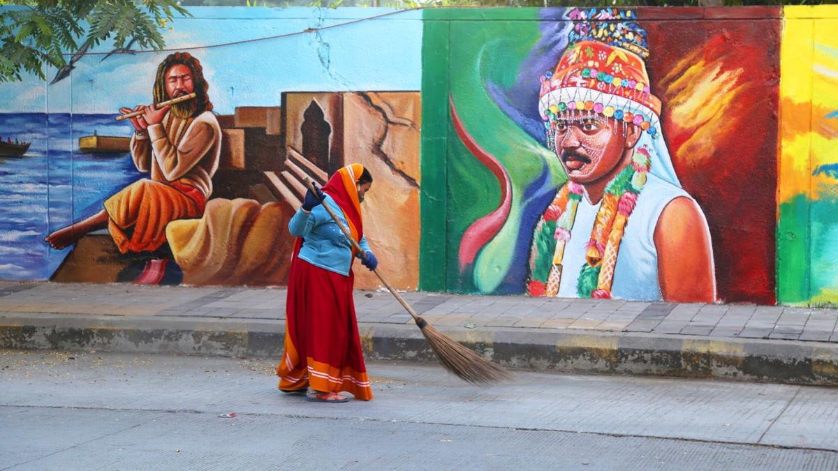Sanitation workers in colorful uniforms with reflective safety gear sweeping street in Indian city