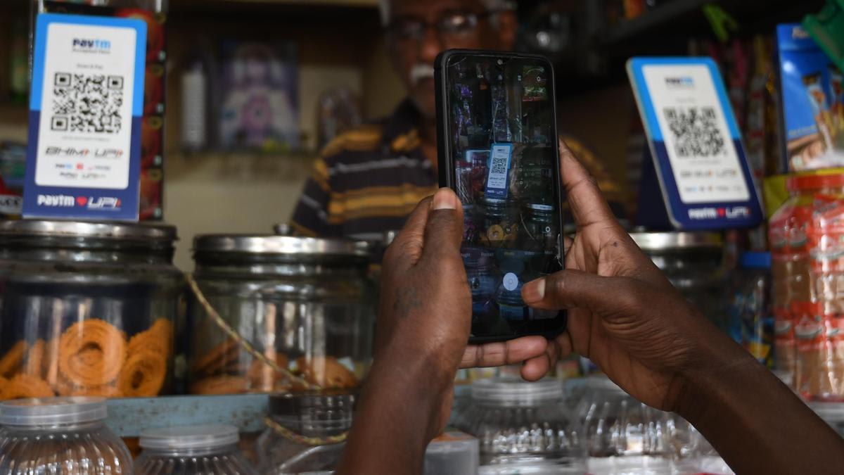 Person using smartphone to make UPI payment at local Indian shop with QR code