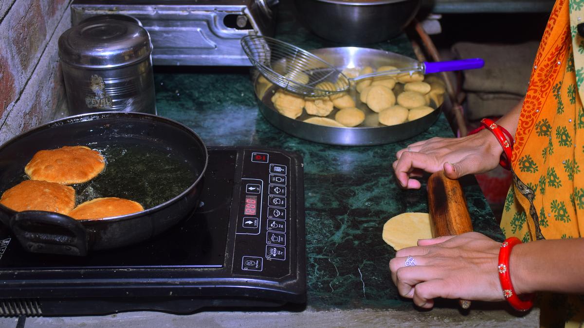 Indian woman cooking on modern induction cooktop in bright kitchen with traditional cookware