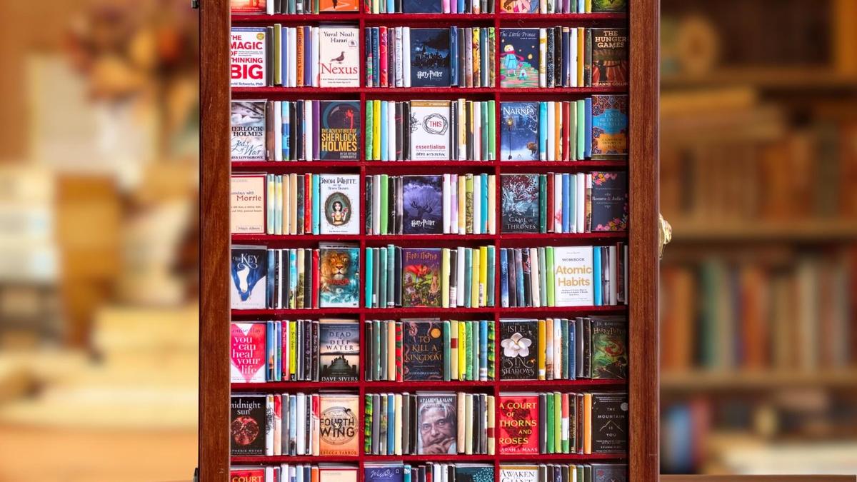 Miniature wooden bookshelf held in hand filled with tiny replica books with detailed covers