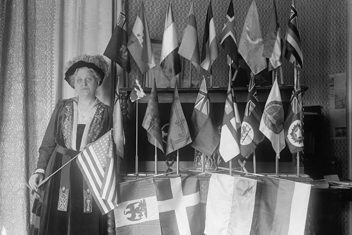 Carrie Chapman Catt standing confidently with flags from 22 nations in 1917