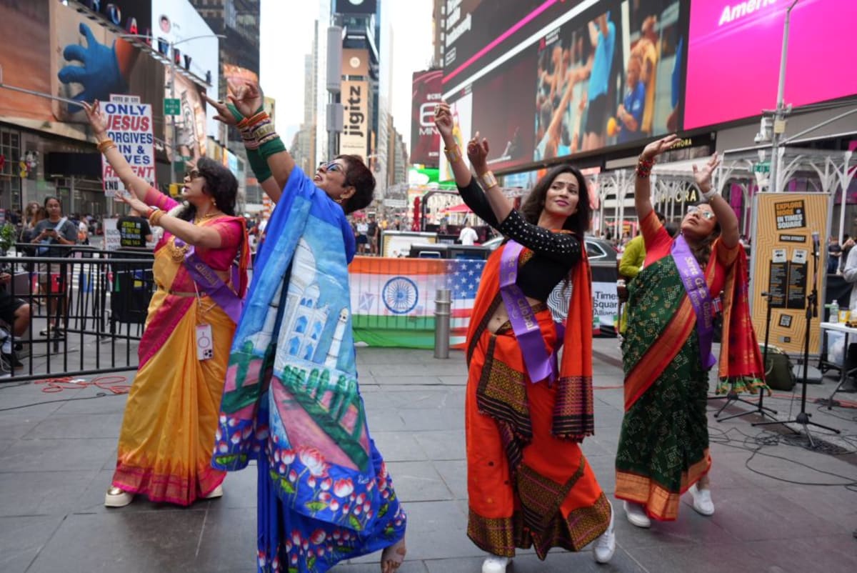 Women in colorful traditional sarees gather beneath international flags in Times Square