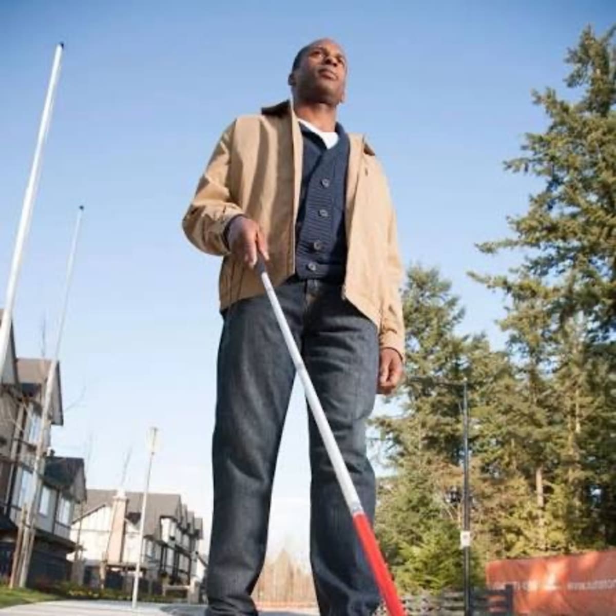 Person using smartphone with earpiece while walking on Nairobi street with mobility cane