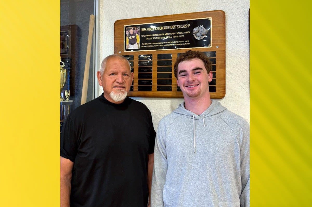 High school senior Samuel Wright standing with former Coach Johnson beside scholarship plaque in gymnasium