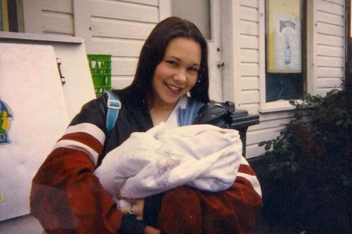 Young teenage mother holding newborn baby standing outside school daycare in 1990s