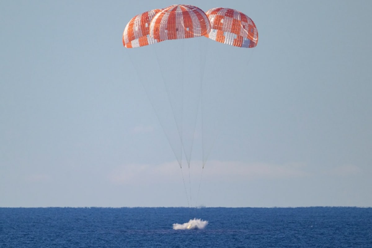 NASA's Orion spacecraft splashing down in the Pacific Ocean at sunset with parachutes deployed