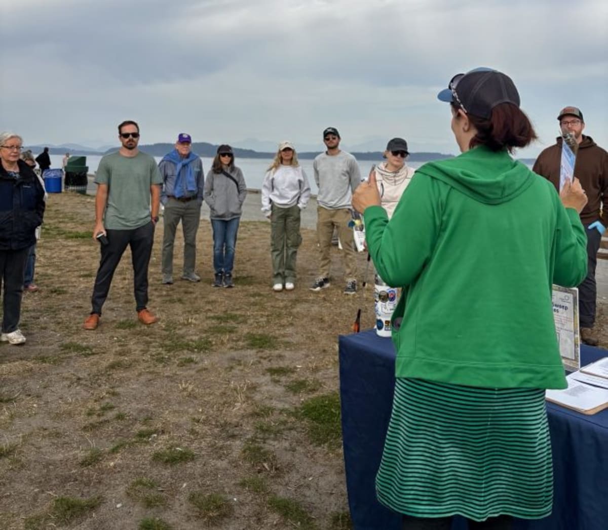 Volunteers in gloves collecting trash and debris along Alki Beach shoreline during community cleanup event