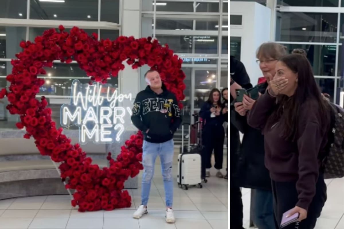 ** Man kneeling with engagement ring at airport arrivals terminal surrounded by red rose heart wreath