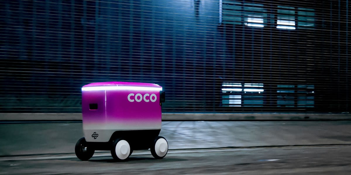 Small delivery robot navigating city sidewalk past buildings using camera-based visual positioning system