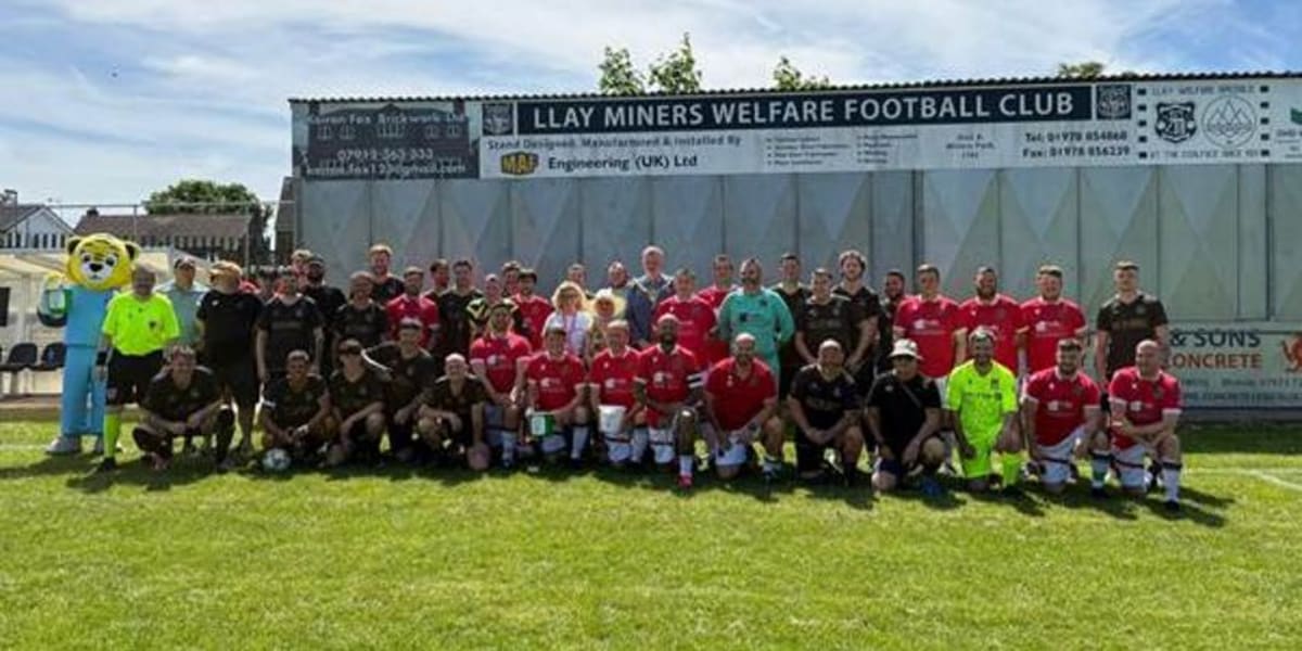 Two football teams compete on green field during charity match for children's hospice fundraiser