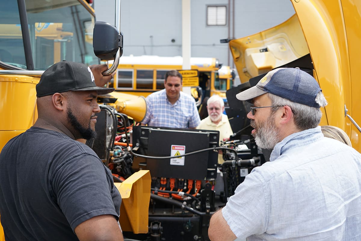 Yellow electric school bus being assembled in modern manufacturing facility with workers