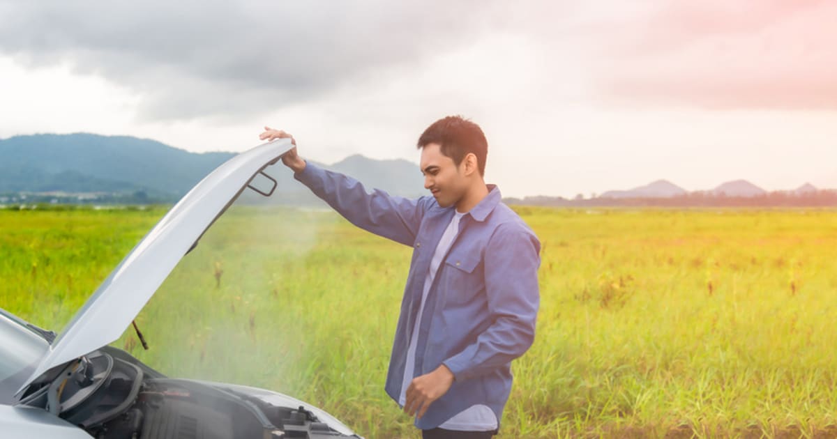 ** Mechanic working under car hood on rural highway shoulder helping stranded motorists