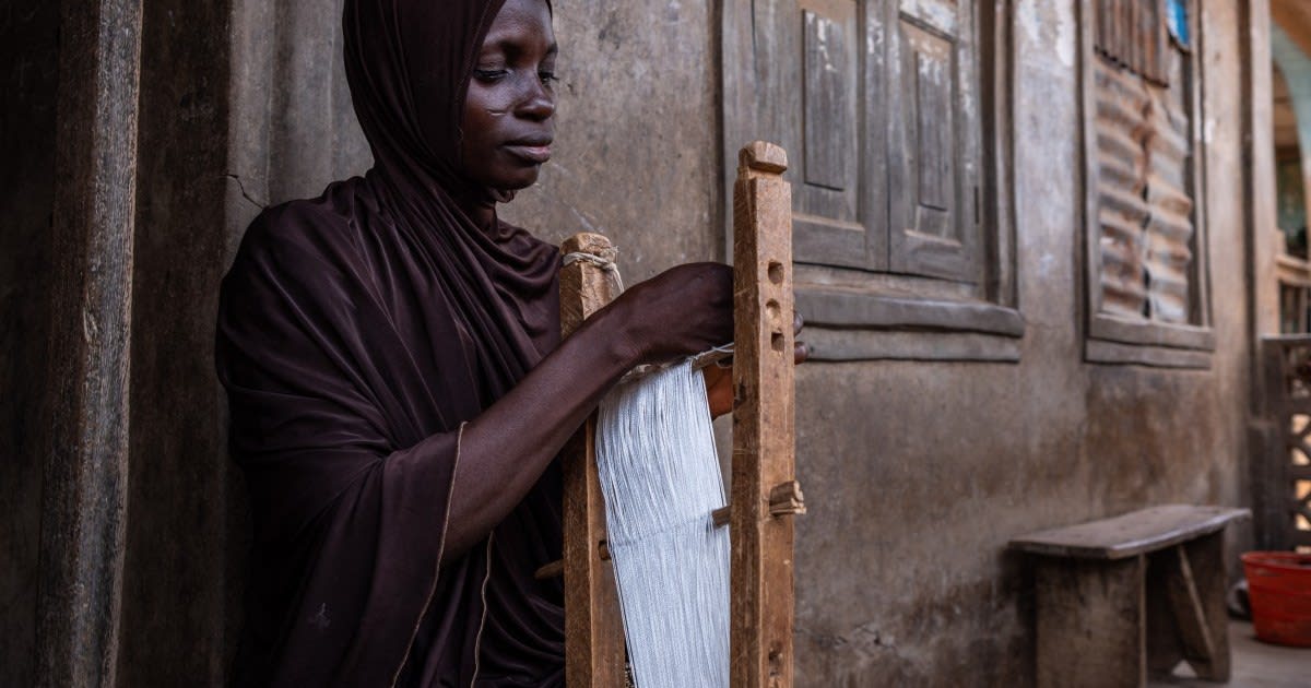 Nigerian weaver working at traditional wooden loom creating colorful aso-oke fabric strips