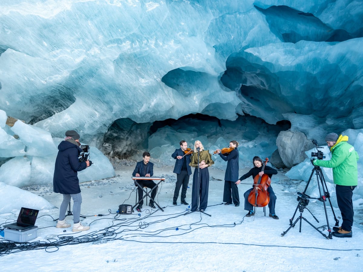 Musician To Athena performing with instruments inside a blue ice cave within melting Swiss glacier