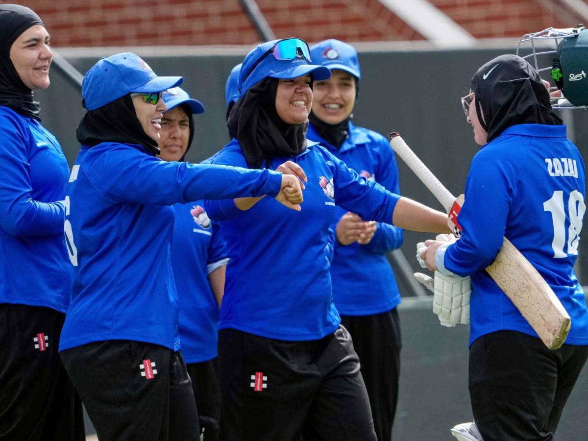 Afghan women cricketers celebrating on field during match in cricket uniforms and equipment