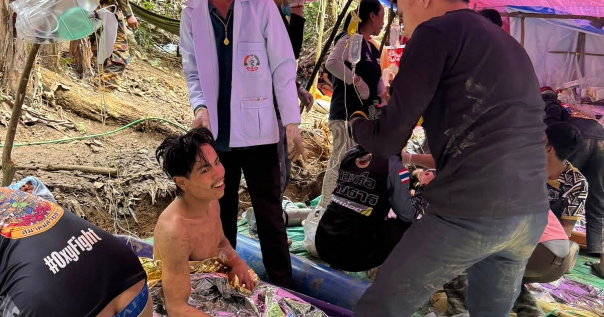 Muddy rescue workers carry survivor on stretcher from flooded cave entrance in Laos