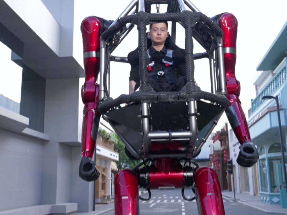 Tall mechanical robot suit with human pilot inside, demonstrating power by breaking through wall