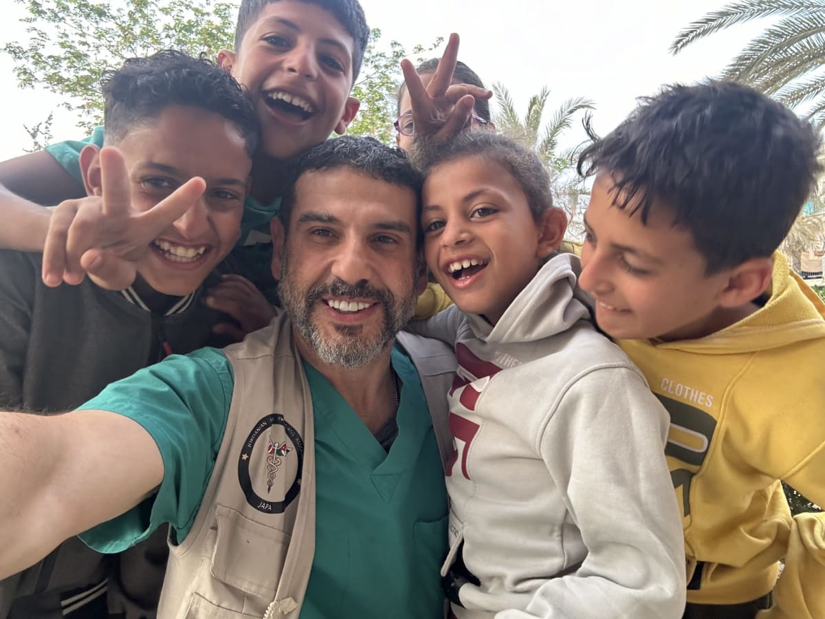 ** Dr. Adam Hamawy in medical scrubs on humanitarian mission, smiling at camera