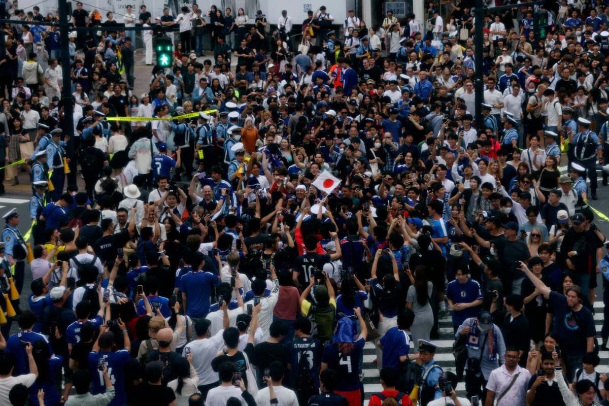 ** Thousands of Japanese soccer fans in blue jerseys celebrating at Tokyo's crowded Shibuya Crossing intersection