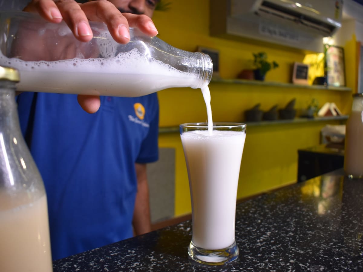 Tall glass of pale milky orchata drink sits on lace-covered table in traditional Goan home