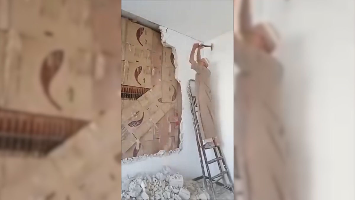 ** Syrian man Abu Bilal standing beside books recovered from behind hidden wall in his home