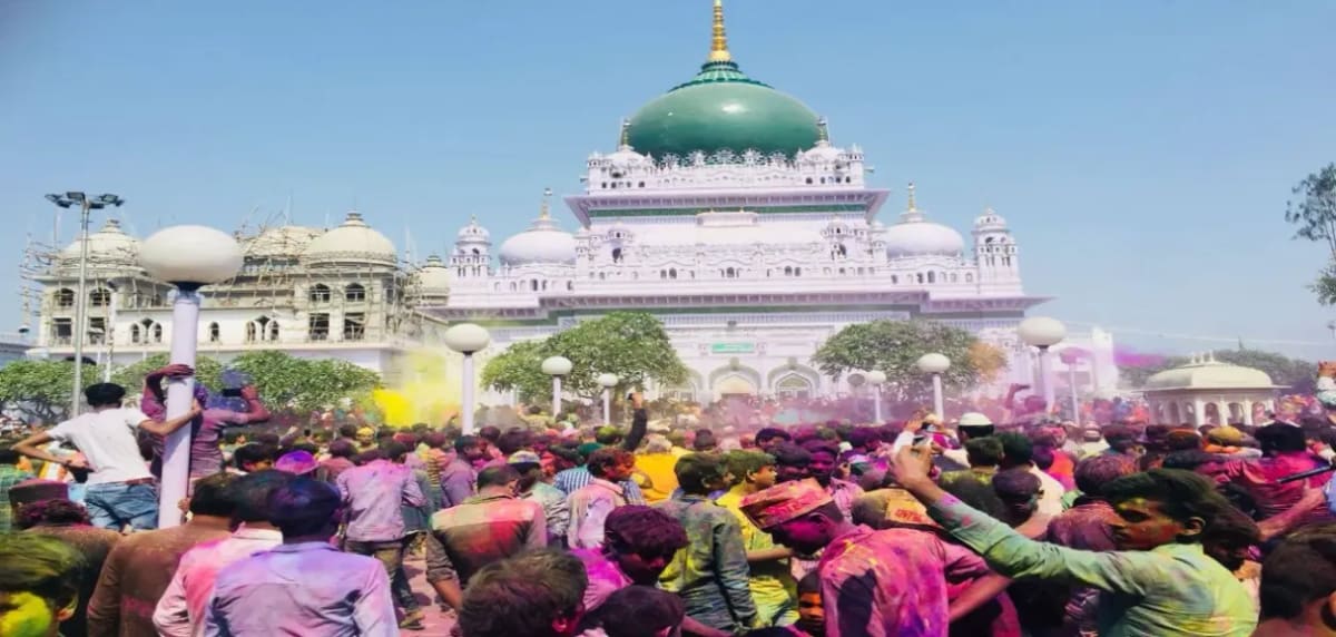 ** Crowds celebrating with colorful powder and rose petals at Dewa Sharif shrine during Holi festival