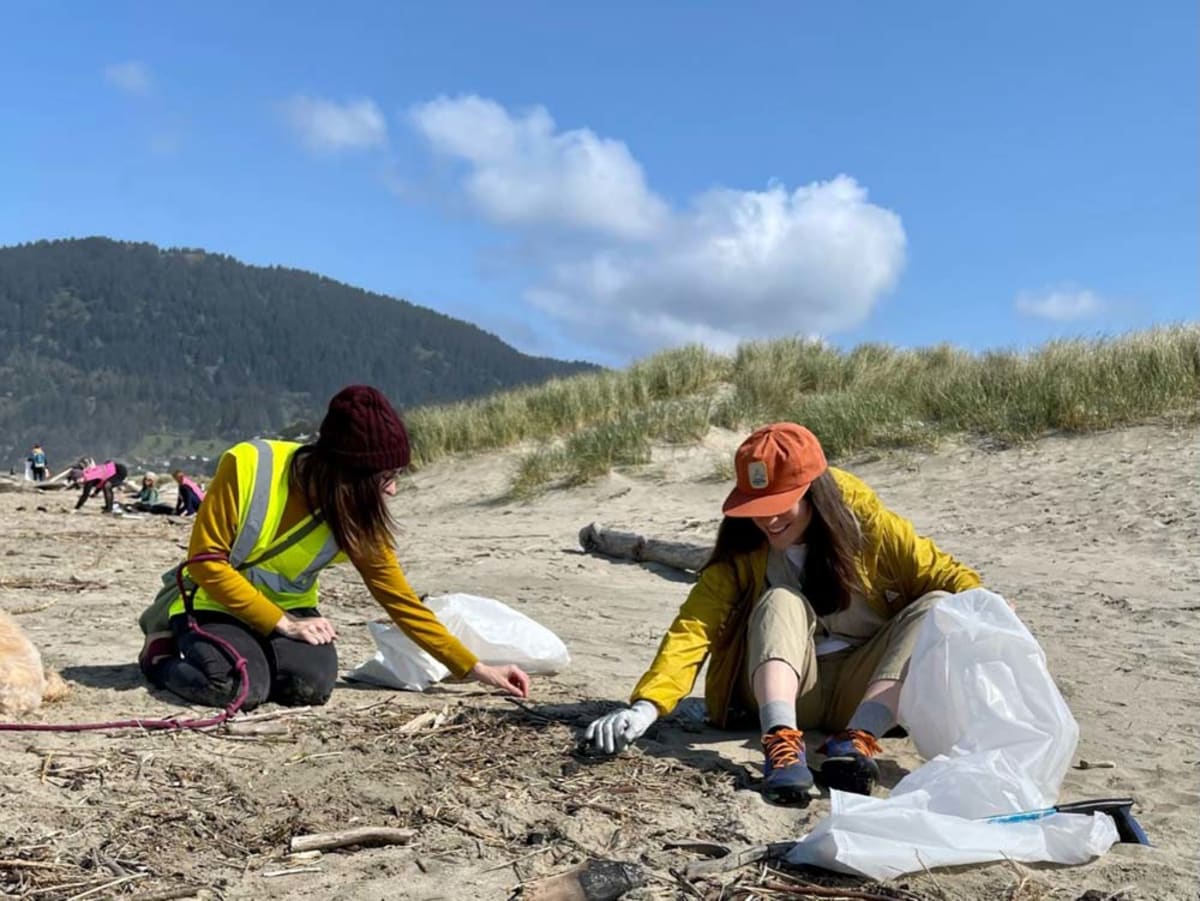 Volunteers with trash bags collecting litter along scenic Oregon coastline beach